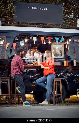 Hipster-Paar bei der Bestellung von Foodtruck auf der Straße; Urban Lifestyle-Konzept Stockfoto
