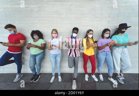 Junge Menschen tragen Gesichtsmaske mit mobilen Smartphone im Freien - multirassische Freunde Spaß mit neuen Technologien Social Media App Stockfoto