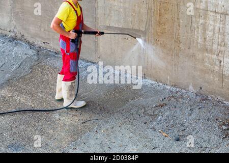 Druckreiniger. Arbeiter reinigt im Freien schmutzigen Beton mit Hochdruck-Wasserstrahl. Stockfoto