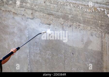 Druckreinigung. Arbeiter reinigt im Freien schmutzigen Beton mit Hochdruck-Wasserstrahl. Stockfoto