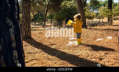 Als Freiwilliger nimmt das kleine Kind Plastikmüll im Wald auf. Kleinkind und kleine Kinder früh Umweltbildungskonzept. Kunststoff frei Stockfoto