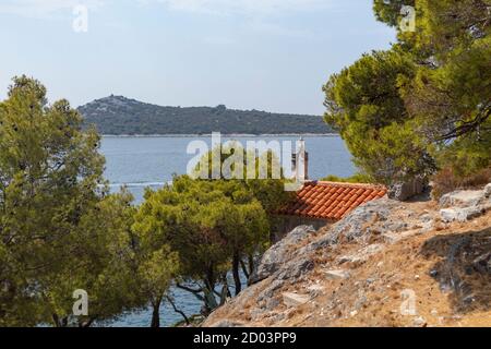 Blick auf kleine Steinkapelle am Rande der Rogoznica Küste, mit Blick auf schöne, blaue Bucht der Adria, umgeben von grünen Pinienwald Stockfoto