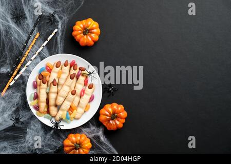Happy halloween Feiertagskonzept. Halloween Handfinger mit Mandelnägeln, Kürbisse, Spinnennetz auf schwarzem Hintergrund. Gruselig hausgemachtes halloween Essen. Stockfoto