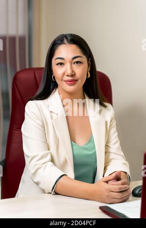 Asiatische Ärztin im weißen Mantel im roten Stuhl sitzend Stockfoto