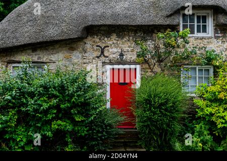 West Lulworth, Vereinigtes Königreich - 19 July 2020: Schönes reetgedeckte Häuschen mit roter Tür und Fensterläden, einzigartiges Dorset buntes Haus Stockfoto