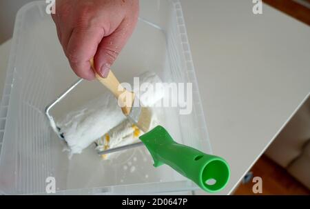 Ein Mann, der einen Pinsel aus einem Behälter mit Malgeräten wie Farbwalzen pflückt. Er wird Unvollkommenheiten an der Wand reparieren. Stockfoto