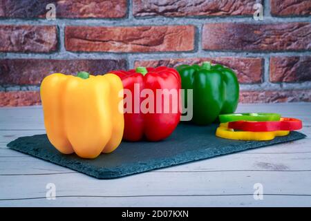 Paprika in verschiedenen Farben, gelb, rot und grün, auf schwarzem Stein Tisch auf einem Holztisch und Ziegelwand. Stockfoto