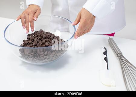 Weibliche Chocolatier hält dunkle Schokolade Couverture Kalbskerne in Glastopf Stockfoto
