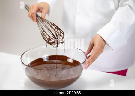 Koch Whisking geschmolzene Schokolade in Glas Rührschüssel mit alten Schneebesen aus Vintage-Draht Stockfoto