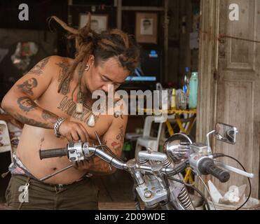 Lampeng, Tahiland - 2019-03-07-Mann mit vielen Tattoos Reparaturen sein Motorrad. Stockfoto