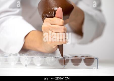 chocolatier Gießen geschmolzene Schokolade in Süßigkeiten Form Herstellung handgefertigten Süßigkeiten Stockfoto