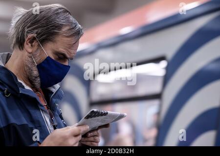 Moskau. Russland. September 28, 2020. Ein Mann in einer schützenden medizinischen Maske steht auf dem Bahnsteig einer U-Bahn-Station und liest sorgfältig eine Zeitung. Der Stockfoto