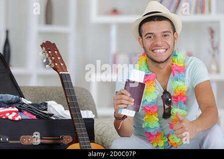 Mann, der seinen Koffer vorbereitet und den Pass mit Daumen nach oben hält Stockfoto