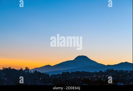 Quito Stadt bei Sonnenaufgang mit Cayambe Vulkan Silhouette, Ecuador. Stockfoto