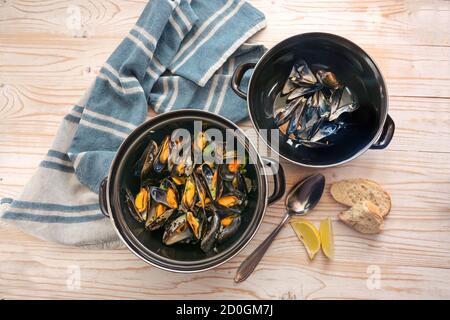 Miesmuscheln im Topf und die leeren Schalen im Deckel, Zitrone, Brot und blaues Handtuch auf einem Holztisch, Kopierraum, Hochwinkelansicht von oben, ausgewählte Focu Stockfoto