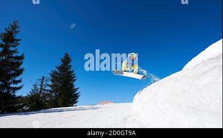 Snowboarder beim Sprung in hohe Berge an sonnigen Tagen gegen blauen Himmel. Skisaison und Wintersportkonzept. Klares Wetter und Himmel, vorbereiteter Schnee Stockfoto