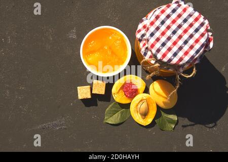 Draufsicht auf Glas mit hausgemachter Bio-Aprikosenmarmelade und reifen Aprikosen und Himbeere auf schwarzem Hintergrund. Platz für Text kopieren Stockfoto