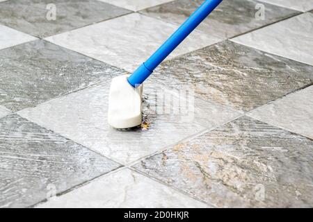 Reinigen Sie den Fliesenboden mit einer Bodenbürste mit langem Griff. Stockfoto