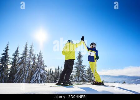 Paare hoch-fünf miteinander unter sonnigen blauen Himmel hoch in den Bergen. Skifahrer nach erfolgreichem Skifahren bis zum Gipfel. Nadelwald auf dem Hintergrund. Glück, Erfolg, gemeinsames Ziel Konzept. Stockfoto