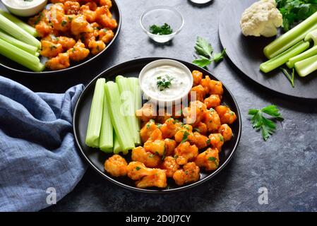 Blumenkohlbüffelflügel mit Sellerie und Sauce auf Teller über blauem Stein Hintergrund. Gesunde Ernährung, pflanzliche Ernährung Konzept. Stockfoto