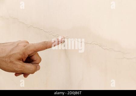 Nahaufnahme der Hand eines Mannes, der auf einen Riss in der Betonwand zeigt. Stockfoto