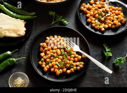 Indische Stil knusprig gerösteten Kichererbsen auf Teller über schwarzem Stein Hintergrund. Vegetarisches veganes Lebensmittelkonzept. Stockfoto