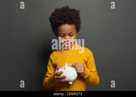 Schwarzes Kind, das in Geldbankmünze setzt Stockfoto