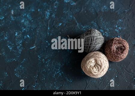 Drei beige grau braune Farbkugeln aus Wollgarn zum Häkeln und Stricken auf dunkelblauem Texture Kitt Beton. Flatlay-Bild mit Platz für Text. Stockfoto