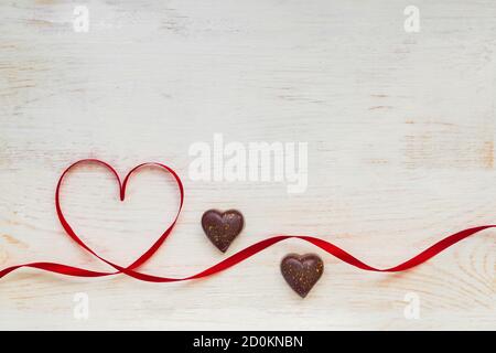 Rotes Geschenk Feier Band in Form von Herz und Schokolade Süßigkeiten auf weißem Holzhintergrund gewellt. Grußkarte mit Kopierplatz für St. Valentines D Stockfoto