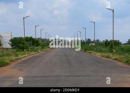 Einsame einsame breite Straße mit schönen Himmel und Straße Lampe ausgerichtet Perspektive, symmetrisch während des Tages, leer wegen Coronavirus Pandemie Stockfoto