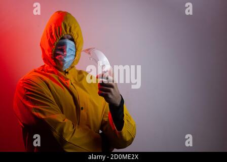 Ein Mann in einem gelben Kapuzenanzug hält eine Schutzbrille, Stockfoto