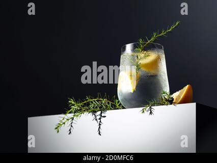 Alkoholgetränk (Gin Tonic Cocktail) mit Zitrone, Wacholderzweig und Eis auf einem dunklen reflektierenden Hintergrund, Kopierraum. Eiscocktail mit Zitrone. Stockfoto
