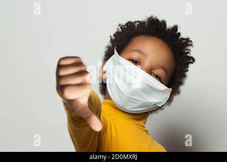 Schwarzes Kind in medizinischen Schutz Gesichtsmaske zeigt Daumen nach unten Auf Weiß Stockfoto