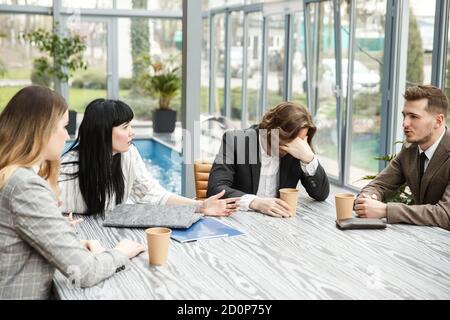 Vier Personen sitzen im Tagungsraum. Einer von ihnen zeigt sich enttäuscht von einer Facepalm Stockfoto