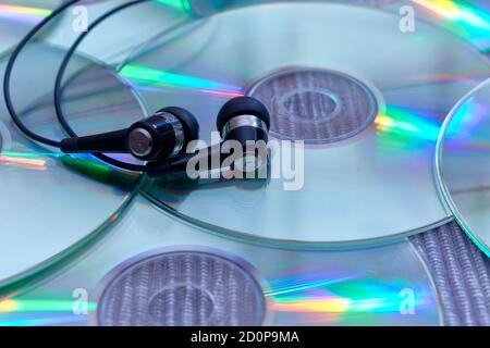 Schwarze Audio-Kopfhörer auf einer Ansammlung von glänzenden CDs Mit farbigen Reflexen Stockfoto
