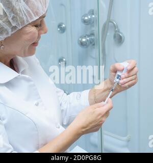 Eine weibliche Kosmetikerin in einer medizinischen Kappe und blauem Latex Handschuhe halten eine Spritze mit einer Injektion Stockfoto