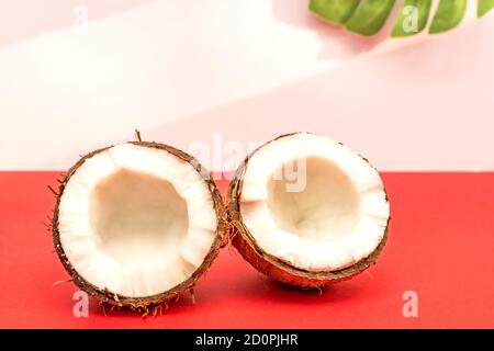 Zwei Hälften frischer roher Kokosnuss auf rotem Hintergrund mit hellen Schatten in Weiß. Stockfoto