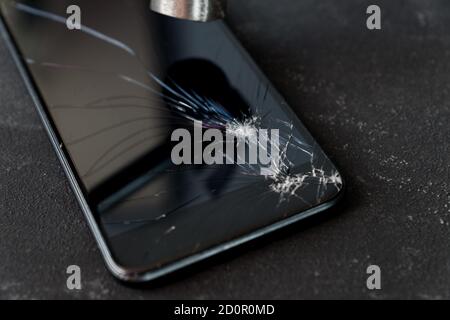 Smartphone mit kaputtem Glasschirm und Hammer auf dunklem Hintergrund. Stockfoto
