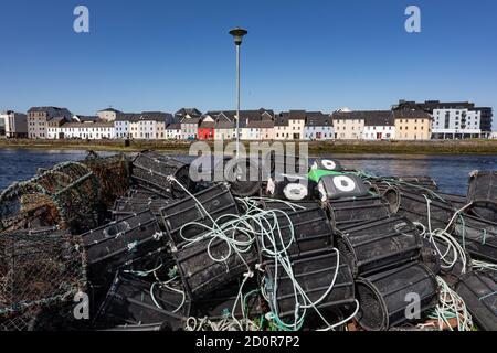 Leere Fischerkrabben Töpfe stapelten sich auf Hafendock mit Blick auf Häuser in der Claddagh Gegend Galway Stadt. Stockfoto