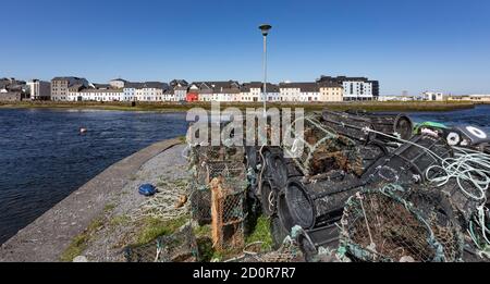 Leere Fischerkrabben Töpfe stapelten sich auf Hafendock mit Blick auf Häuser in der Claddagh Gegend Galway Stadt. Stockfoto