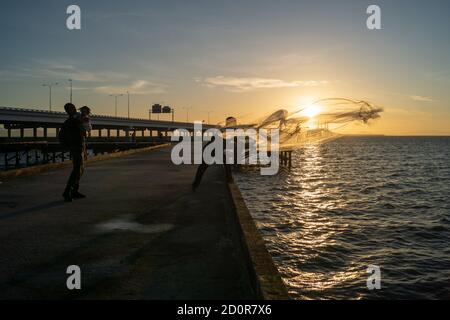 Batu Maung, Penang/Malaysia - Jan 01 2020: Ein Mann, der Netz ins Meer wirft. Ein anderer Mann umarmte ein Kind. Stockfoto