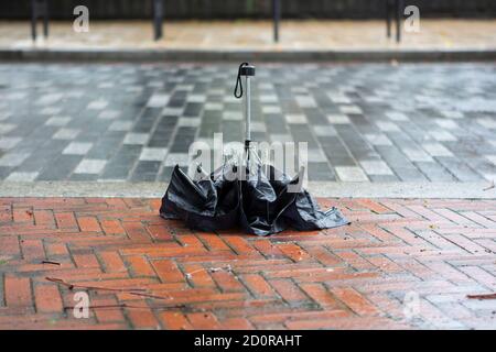 Verlassene schwarze Regenschirm auf einem nassen Bürgersteig Stockfoto