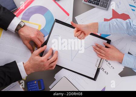 Geschäftsfrau zeigt Daumen nach oben über Tisch mit Finanzcharts. Stockfoto