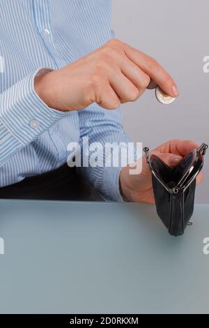 Womans Hand setzen eine Münze in eine schwarze Handtasche. Stockfoto