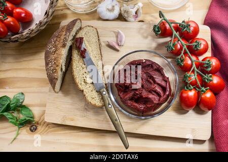 Draufsicht Stillleben mit einer Schüssel konzentrierter Tomatensauce, Vollkornbrot, einem Bündel Piccadilly Tomaten, Knoblauch und Basilikum Stockfoto