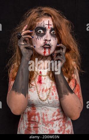 Eine junge Frau mit roten Haaren und Profi-Make-up gruselig aussehen, trägt blutig weiße Kleidung. Halloween-Konzept Stockfoto