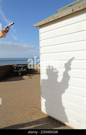 Silhouette eines Mannes, der in der Nähe des weißen Holzstrandes Gewehr hält Hütte Stockfoto
