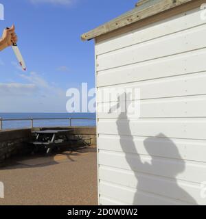 Silhouette eines Mannes, der Messer in der Nähe der weißen Strandhütte hält Stockfoto