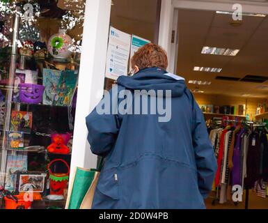 Ältere Frau trägt Gesichtsbedeckung suchen in Ovens Hospices Charity Shop Fenster. Hockley, Essex, Großbritannien Stockfoto