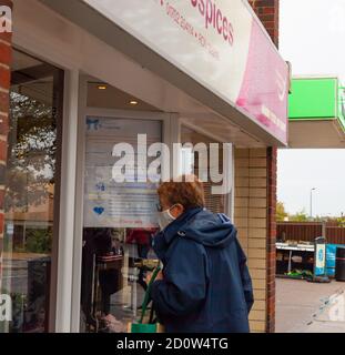 Ältere Frau trägt Gesichtsbedeckung suchen in Ovens Hospices Charity Shop Fenster. Hockley, Essex, Großbritannien Stockfoto